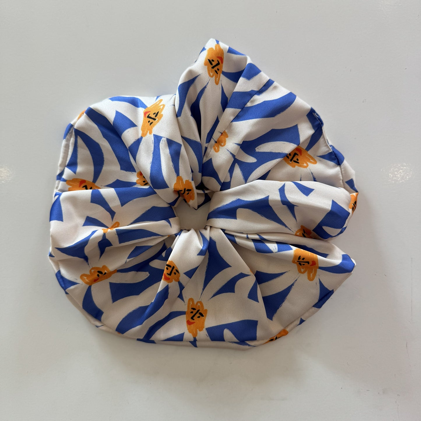 Maxi chouchou satiné avec imprimés de marguerites blanches sur fond bleu.