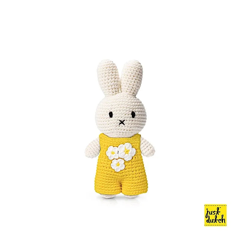 Peluche en crochet Miffy avec une salopette jaune et des fleurs blanches.