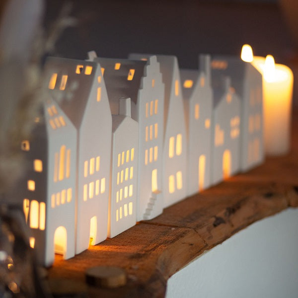 Plusieurs photophores en porcelaine en forme de maison alignés sur une étagère.