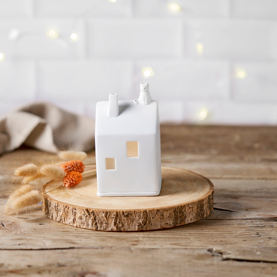 Photophore en porcelaine blanche en forme de maison avec un chat sur le toit.