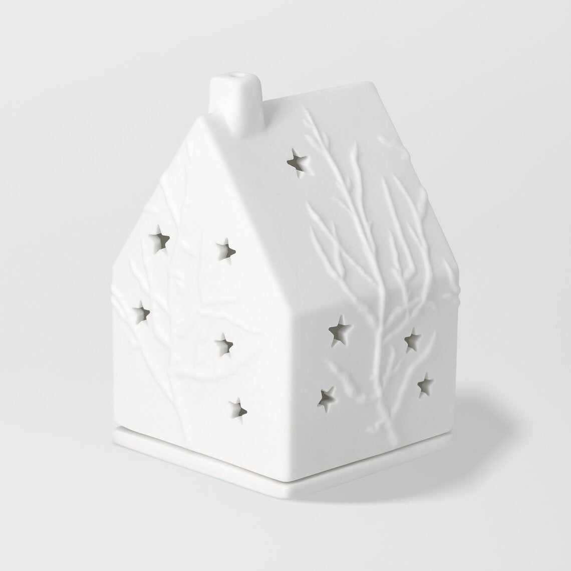 Photophore en porcelaine blanche en forme de maison constellé d'étoiles et d'arbres.