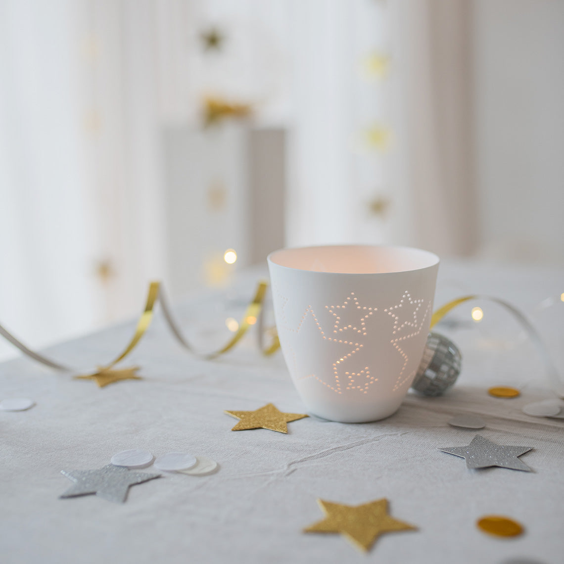 Photophore rond en porcelaine blanche avec des étoiles découpées.