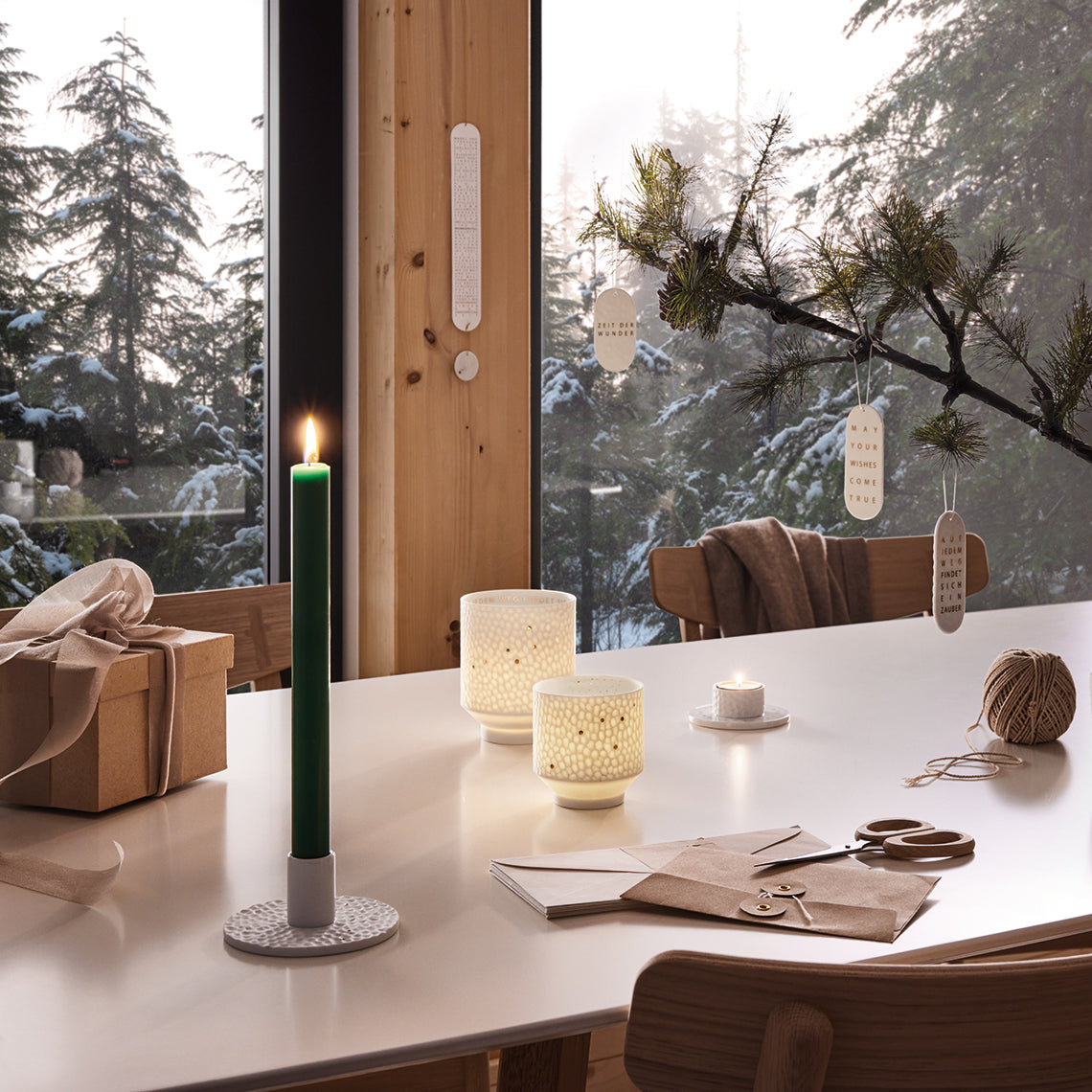 Photophores ronds en porcelaine blanche martelée avec une étoile filante et une constellation dorée, posés sur une table dans un décor enneigé.