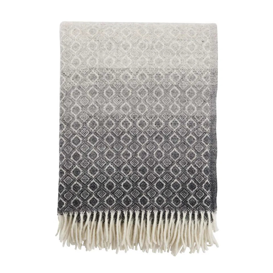 Plaid en laine d'agneau avec des motifs blancs sur un fond dégradé gris.