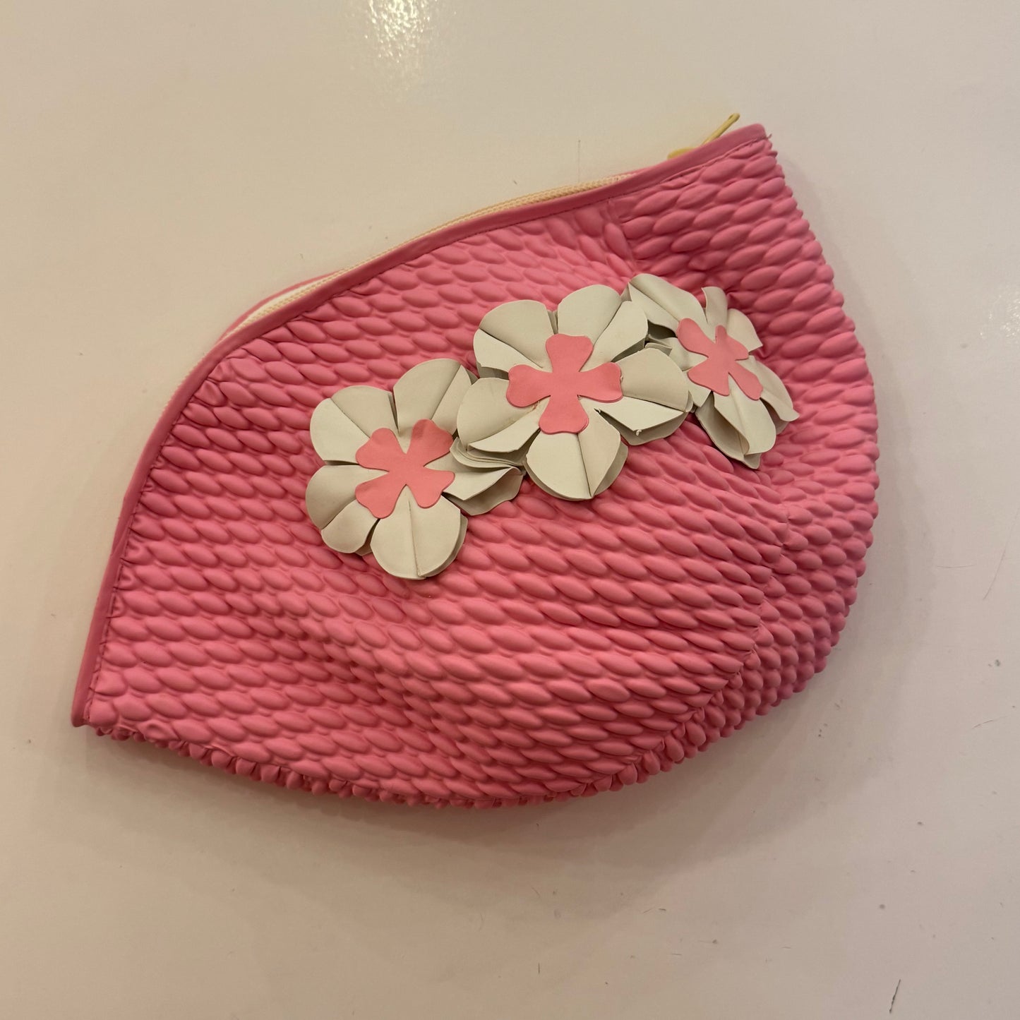 Trousse de toilette en forme de bonnet de bain rose avec des fleurs blanches.