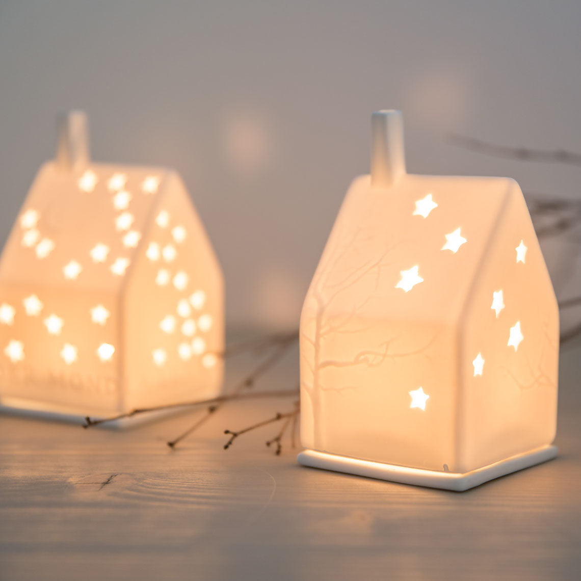 Photophore en porcelaine blanche en forme de maison constellé d'étoiles et d'arbres.