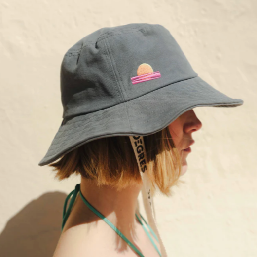 Femme de profil portant un bob bleu gris 23 degrés avec broderie coucher de soleil 