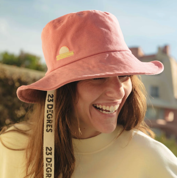 Femme portant un bob rose brodé d'un coucher de soleil dans les tons jaunes avec un ruban avec logo 