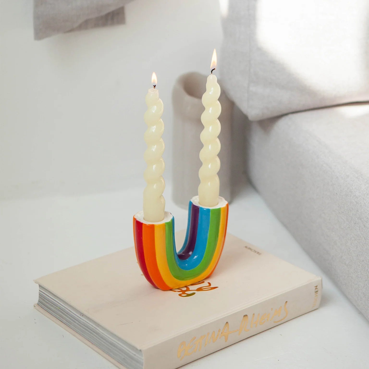 Bougeoir double en céramique en forme d'arc-en-ciel renversé avec deux bougies torsadées blanches.