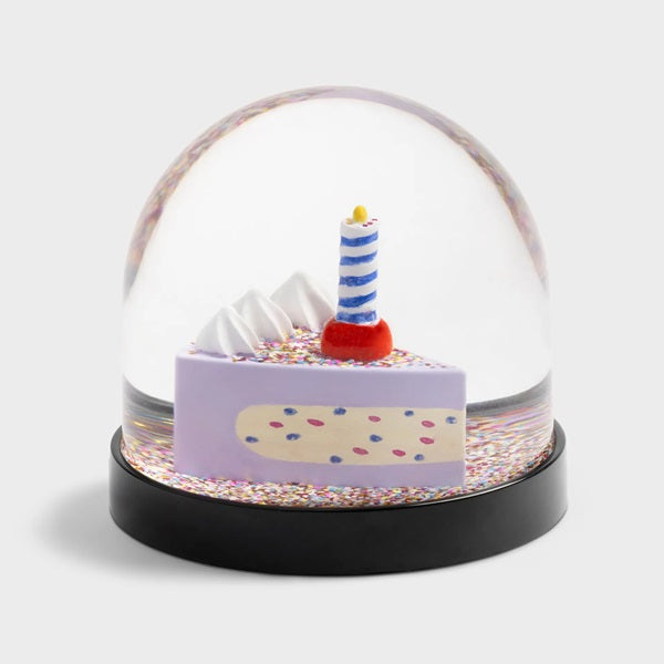 Boule à neige Klevring, avec une part de gâteau avec une bougie sous des confettis multicolores.