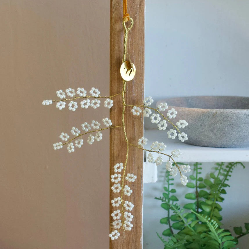 Branche à suspendre en fils dorés torsadés avec fleurs de perles blanches.