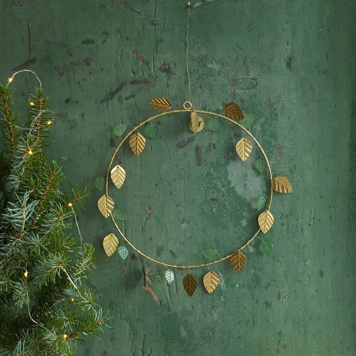 Couronne en fils dorés avec des feuilles dorées et vertes, à poser ou à suspendre en décoration de Noël. 