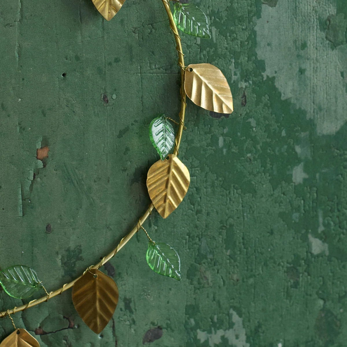 Couronne en fils dorés avec des feuilles dorées et vertes, à poser ou à suspendre en décoration de Noël. 