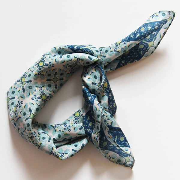 Foulard carré en soie avec motif floral en mosaïque, dans les tons bleu clair, bleu foncé et des touches de jaune et vert clair. 