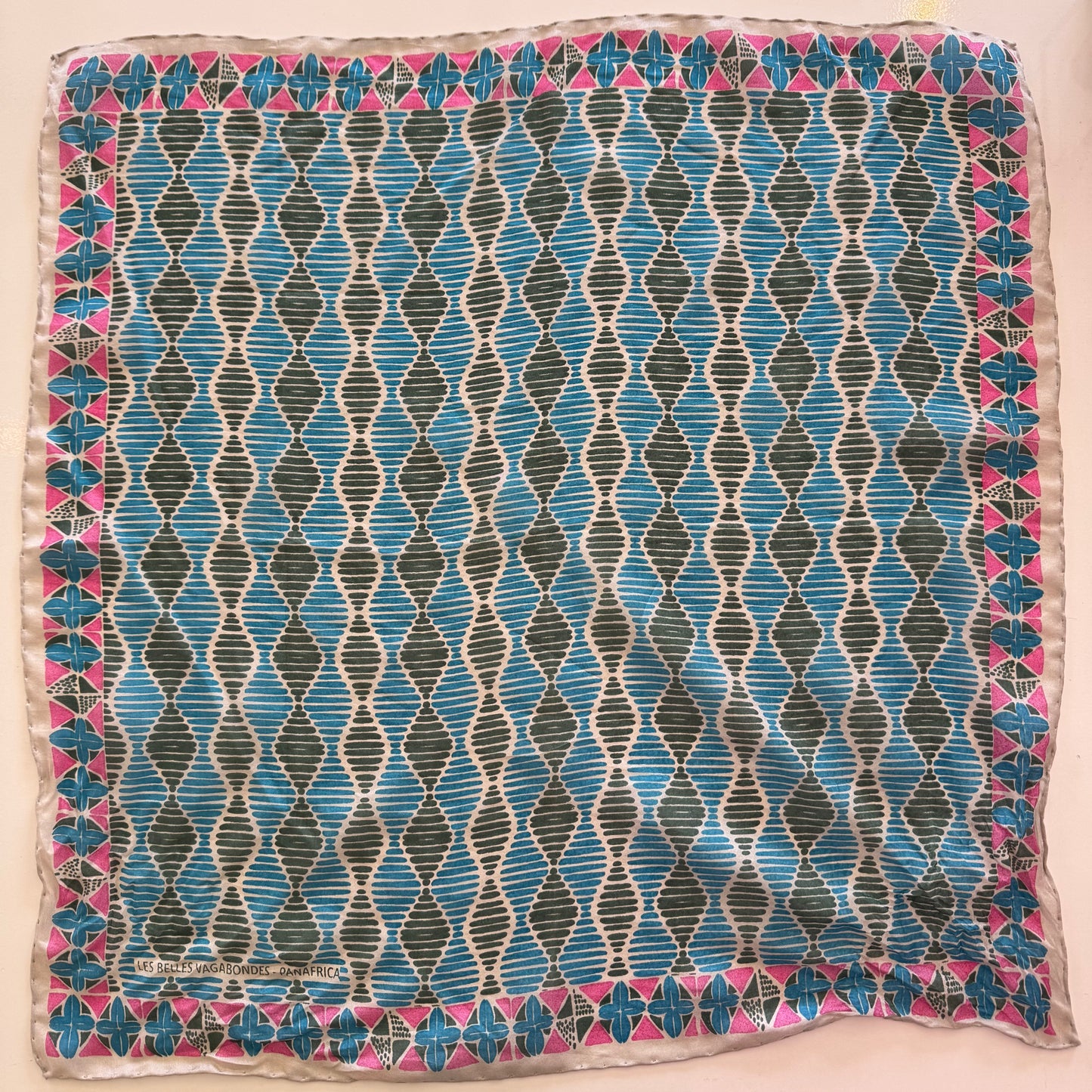 Foulard carré en soie avec motif géométrique type africain, dans les tons bleu, vert et rose.
