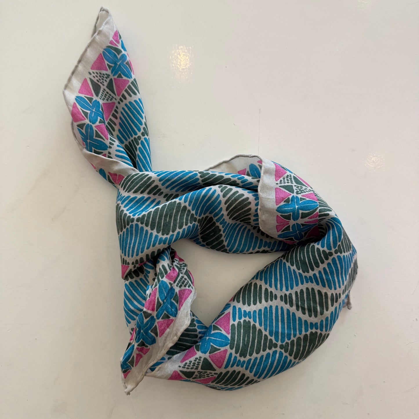 Foulard carré en soie avec motif géométrique type africain, dans les tons bleu, vert et rose.