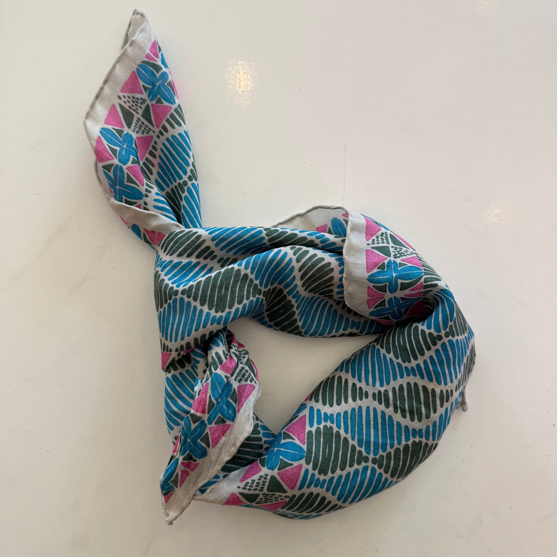 Foulard carré en soie avec motif géométrique type africain, dans les tons bleu, vert et rose.