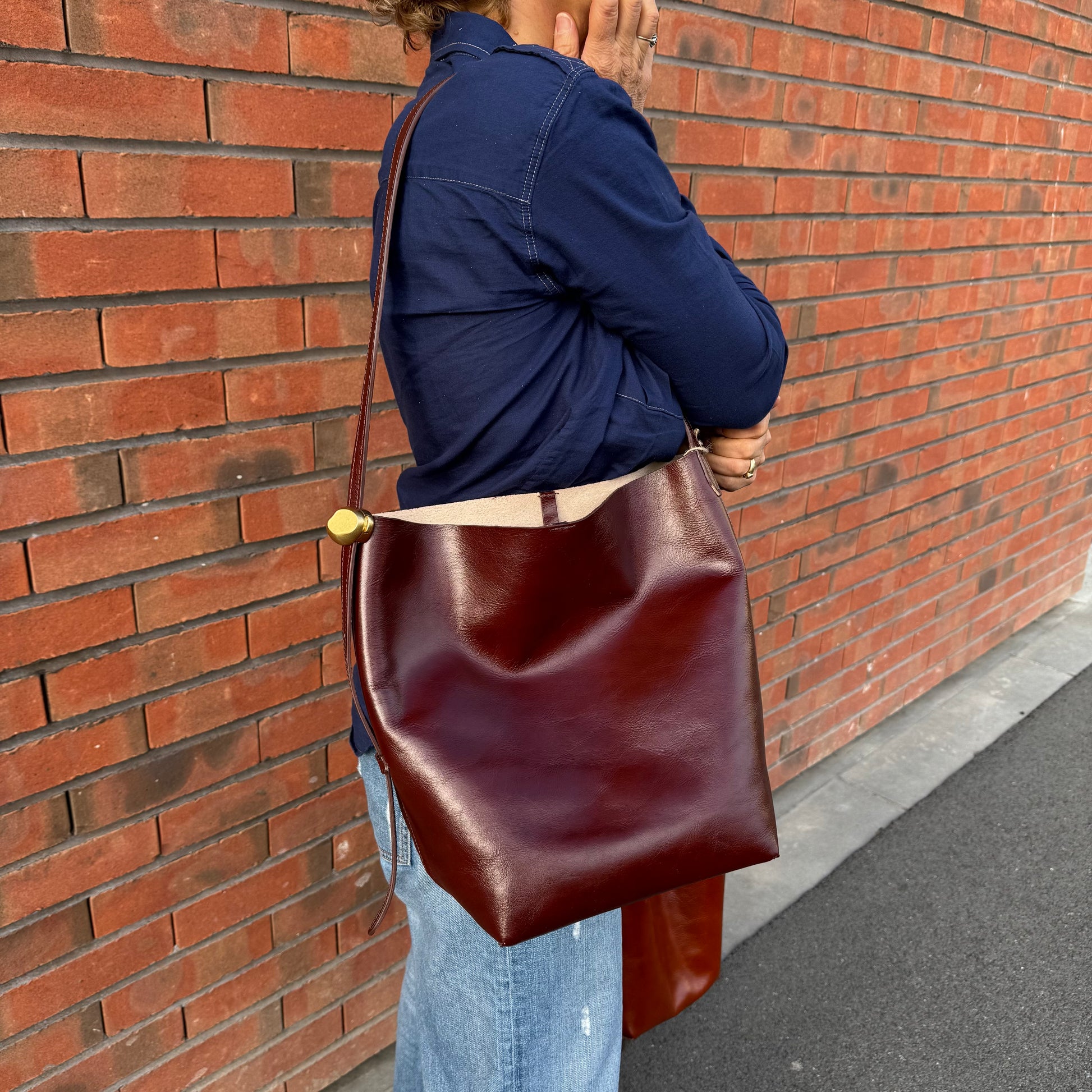 Grand sac seau en croute de cuir, porté épaule, coloris marron chocolat. 