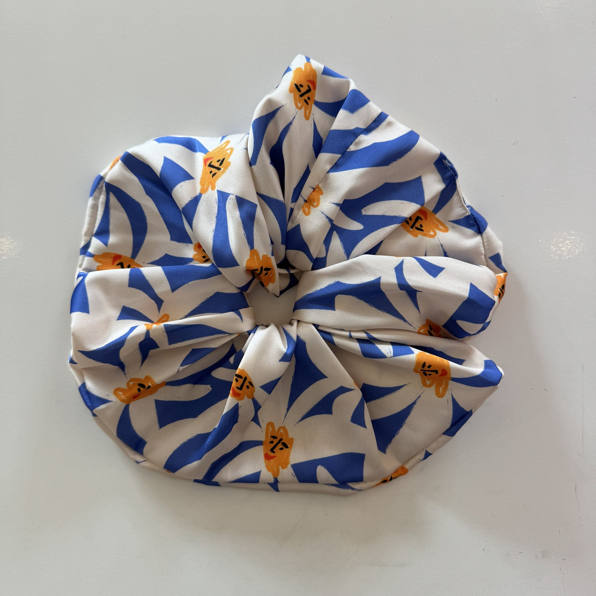 Maxi chouchou satiné avec imprimés de marguerites blanches sur fond bleu.