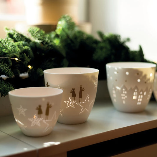 Plusieurs photophores ronds en porcelaine blanche avec des anges dorés et des étoiles perforées.