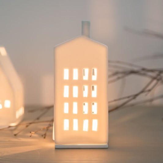 Petit photophore en porcelaine blanche en forme d'immeuble allumé.