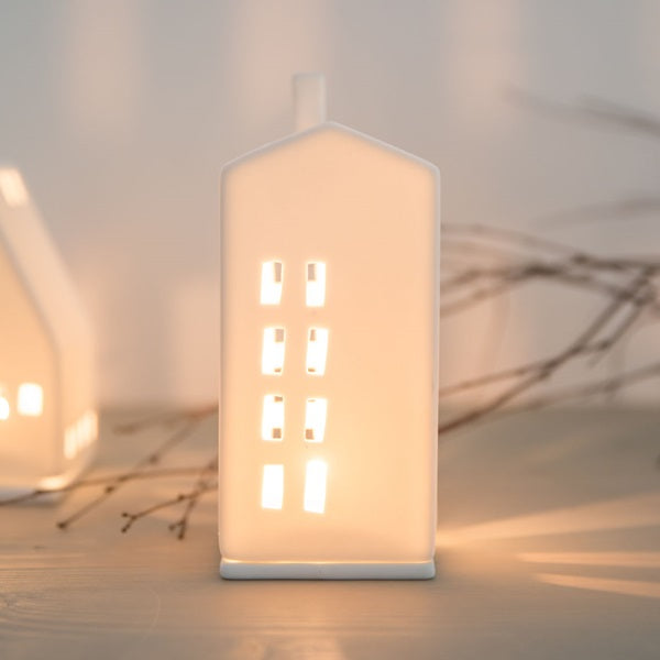 Petit photophore en porcelaine blanche en forme d'immeuble allumé.