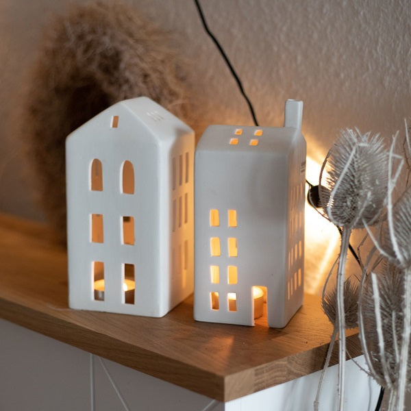 Petit photophore en porcelaine blanche en forme d'immeuble allumé, à côté d'un autre photophore.