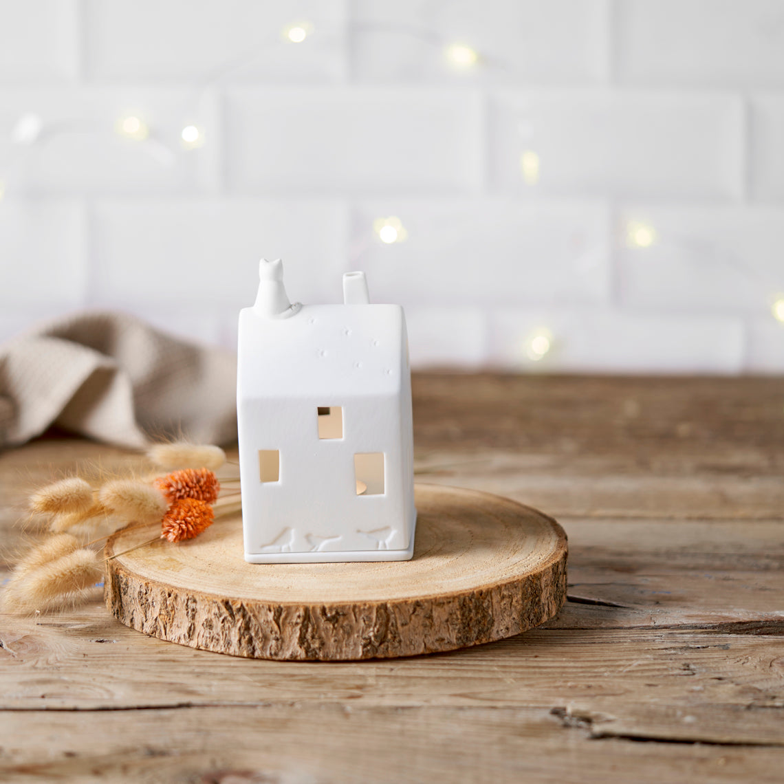 Photophore en porcelaine blanche en forme de maison avec un chat sur le toit.