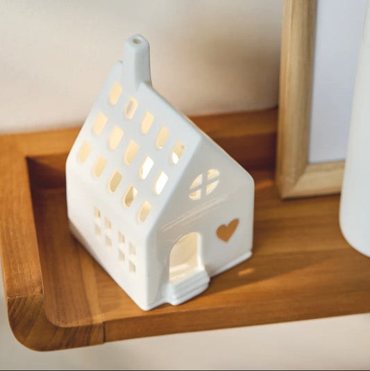 Photophore en porcelaine blanche ajourée en forme de maison, avec un coeur doré en façade.