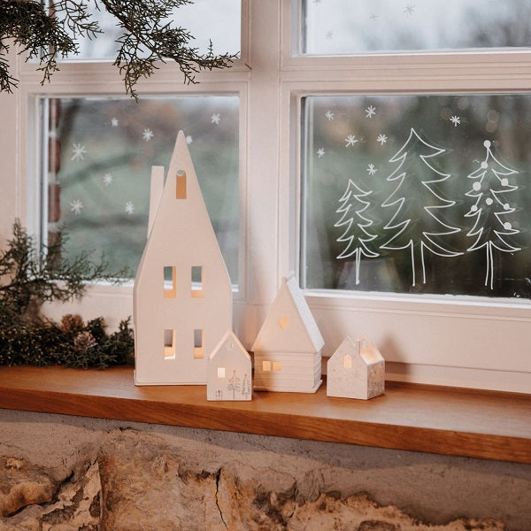 Photophore en porcelaine blanche en forme de maison avec un grand toit pentu, format XL à côté d'autres petites maisons en photophores.