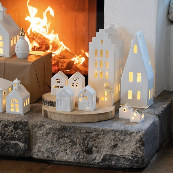 Photophore en porcelaine blanche en forme de maison avec un grand toit pentu, format XL à côté d'autres maisons en porcelaine de différentes tailles pour donner une notion d'échelle.