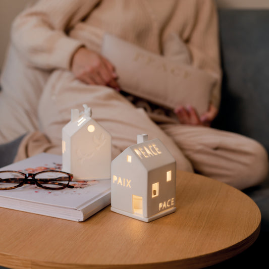 Photophore en porcelaine blanche en forme de maison avec écrit le mot "Paix" en plusieurs langues.