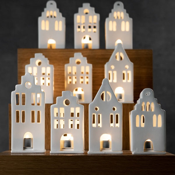 Photophore en porcelaine blanche en forme de maison avec un toit flamand, à côté d'autres maisons flamandes.