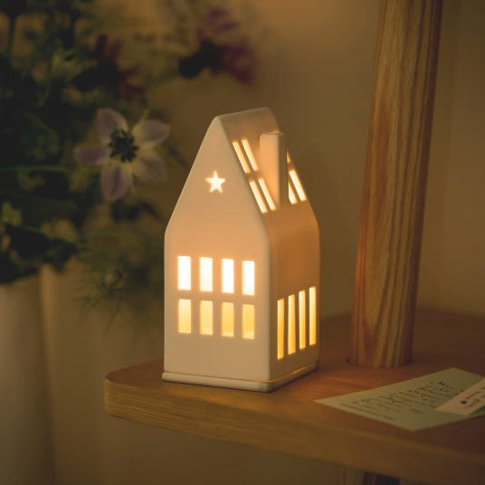 Photophore en porcelaine blanche en forme de maison avec le toit pointu et une ouverture en étoile.