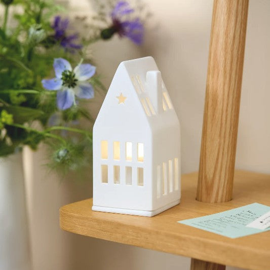 Photophore en porcelaine blanche en forme de maison avec le toit pointu et une ouverture en étoile.