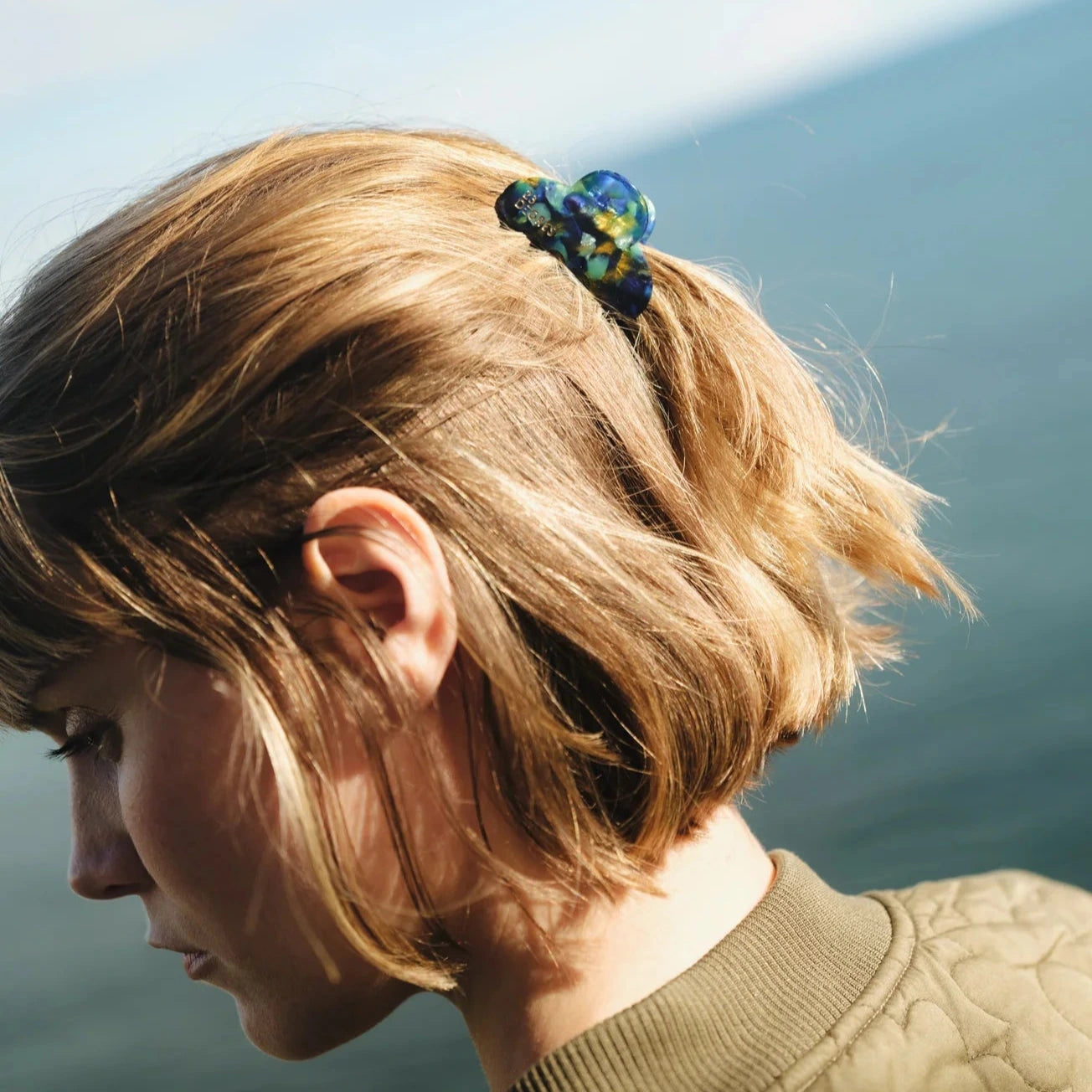 Petite pince à cheveux en forme de nuage à motifs écaille, coloris bleu et vert, portée en demi-queue sur cheveux courts. 