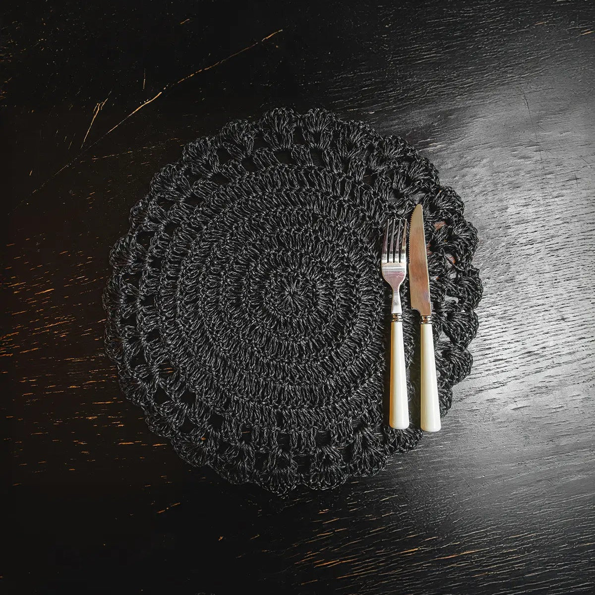 Set de table rond en raphia noir avec des détails au crochet, posé sur une table.