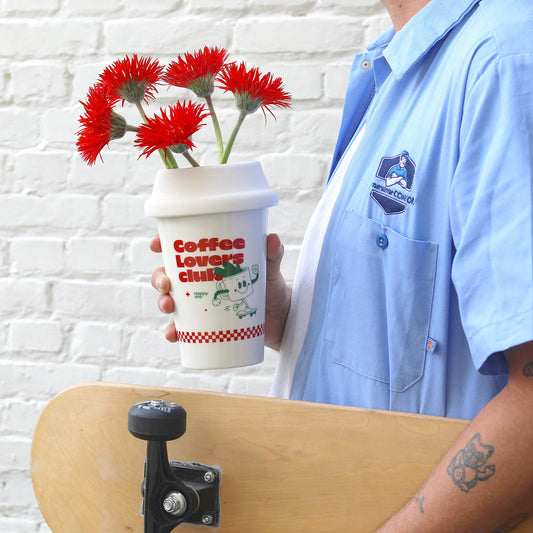Vase en céramique en forme de tasse à café à emporter en blanc avec des inscriptions rouges et vertes.