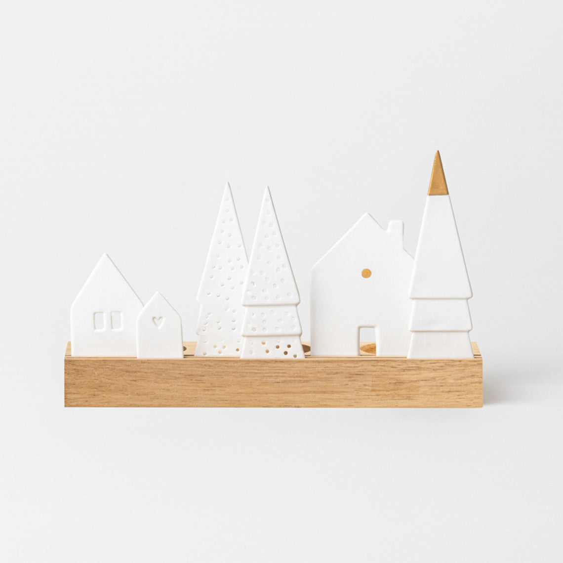 Village de Noël en porcelaine ponctué de doré sur socle en bois rainuré. 