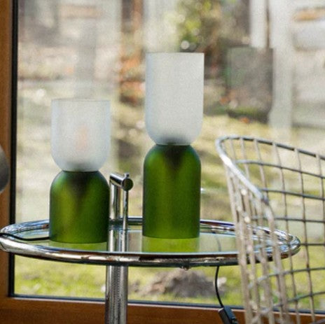 Deux lampes en verre recyclé vert foncé de la marque Q de bouteilles posées sur une table 