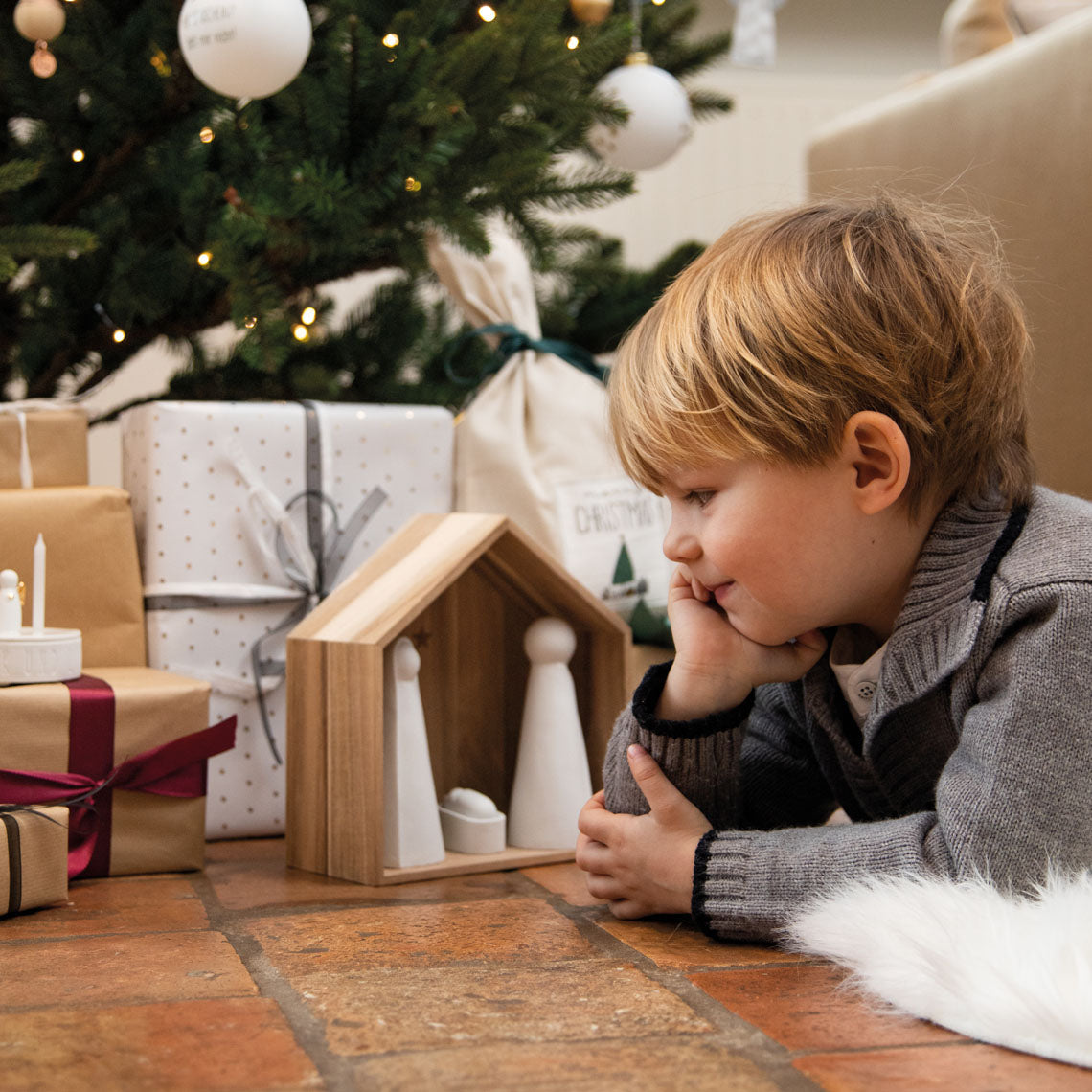 Grande crèche en bois abritant trois figurines en porcelaine, sous un sapin.