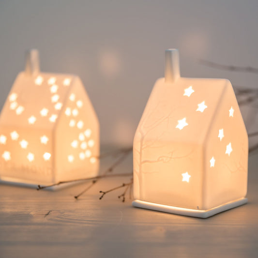 Photophore en porcelaine blanche en forme de maison constellé d'étoiles et d'arbres.