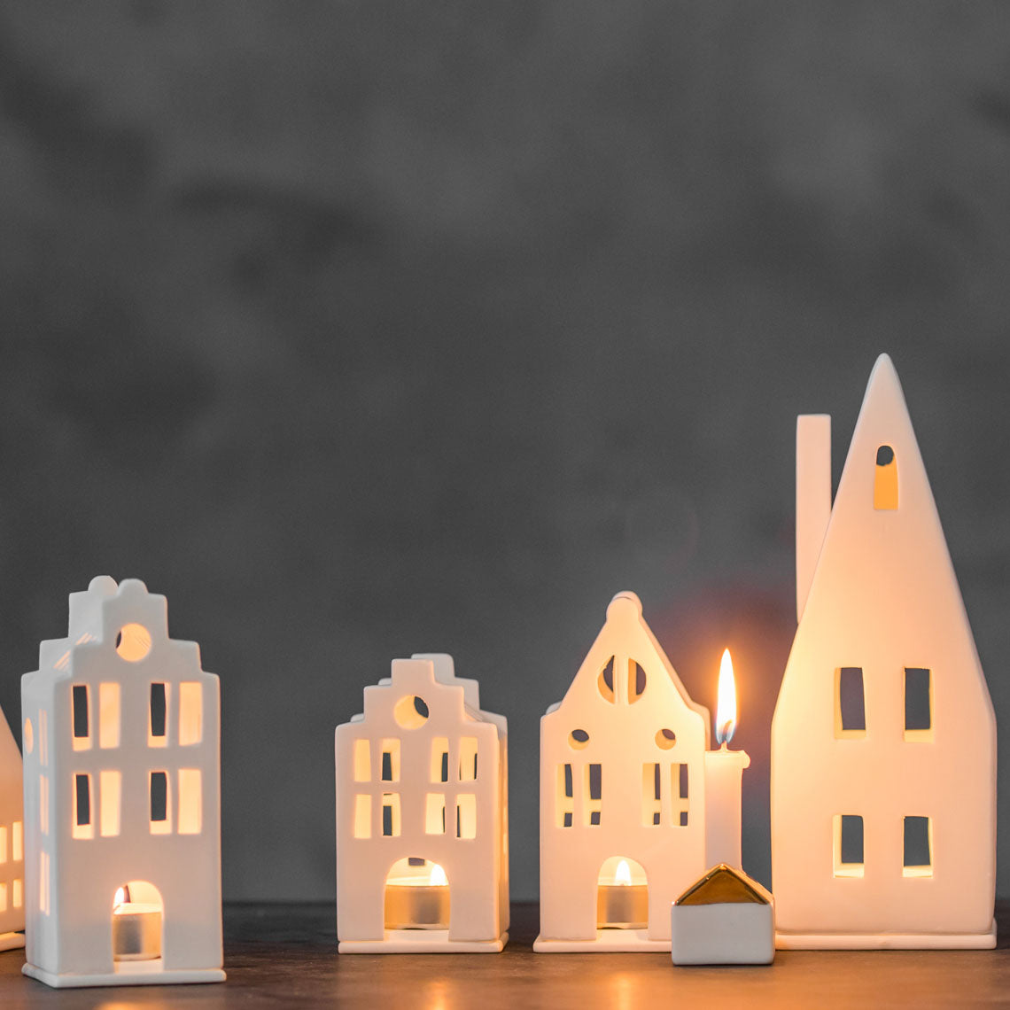 Photophore en porcelaine blanche en forme de maison avec un grand toit pentu, au côté d'autres petites maisons en porcelaine.