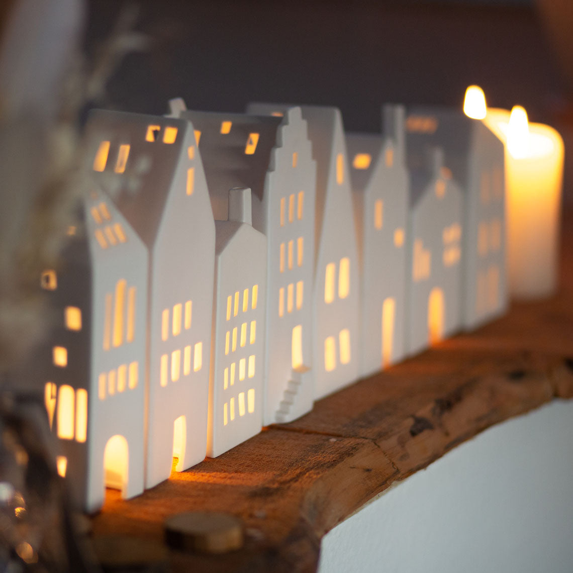 Photophore en porcelaine blanche en forme de maison avec un grand toit pentu, aligné sur une étagère avec d'autres photophores en forme de maison.